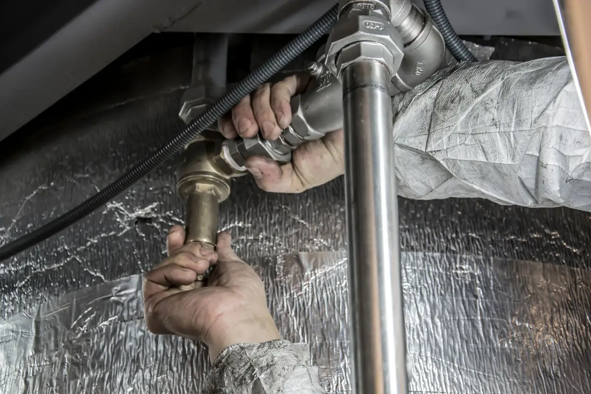 Plumber inspecting pipework under a sink for a water leak